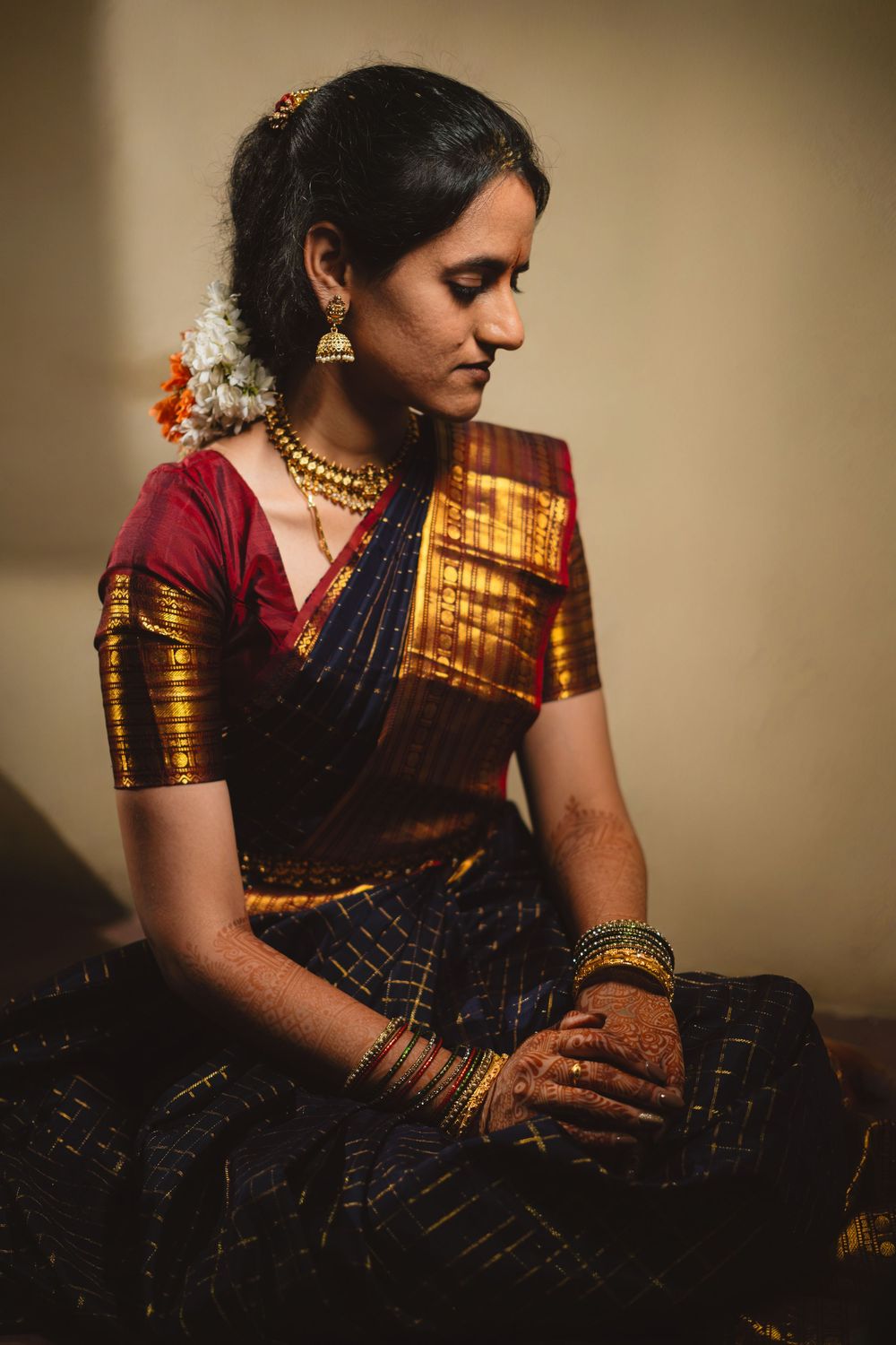 Elegant South Indian traditional fashion with gold-bordered navy silk saree and maroon blouse adorned with jewelry in soft lighting.