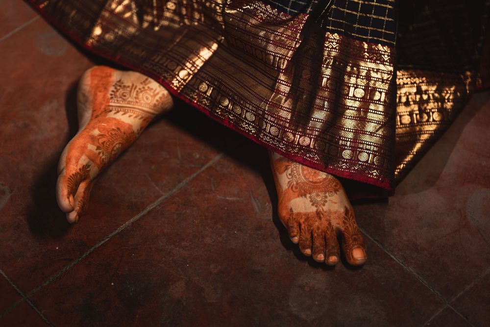Henna-decorated feet rest on a dark tiled floor beside traditional fabric with intricate designs.