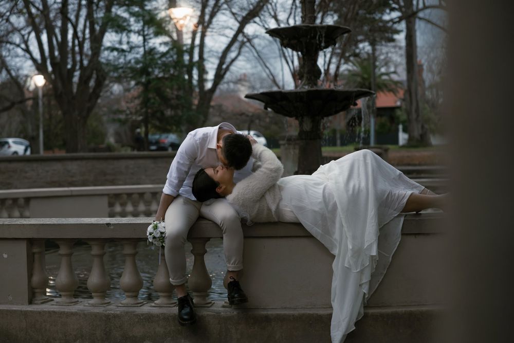 A couple shares an intimate moment on stone railings near a fountain during twilight hours.