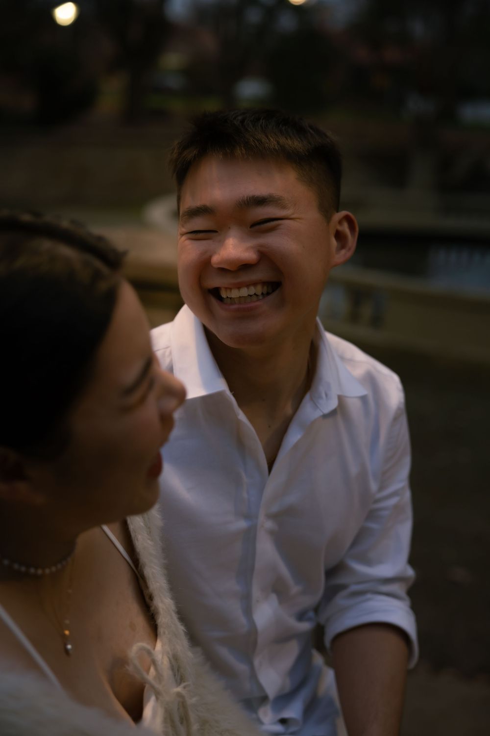 A couple in white outfits share tender romantic moments together at dusk in an outdoor setting.