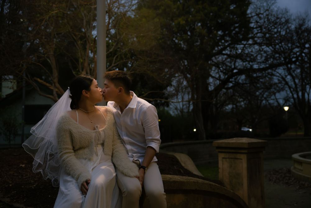 Two people share a romantic moment under the evening sky in an outdoor garden setting.