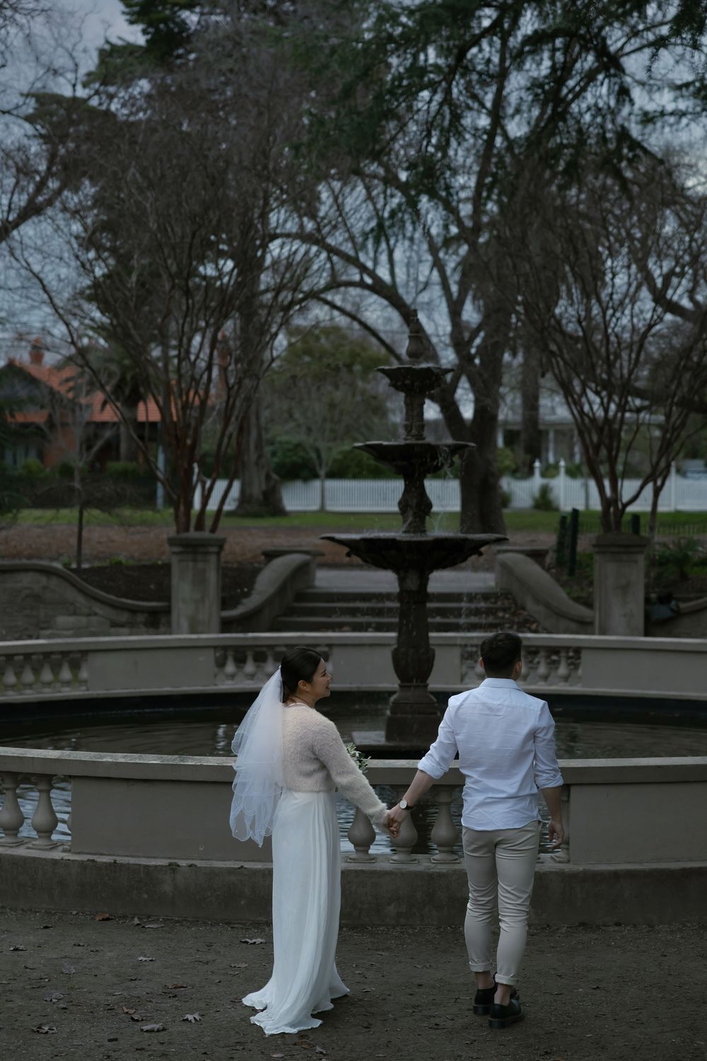 A couple stands by a vintage fountain in a misty garden setting during a romantic twilight moment.