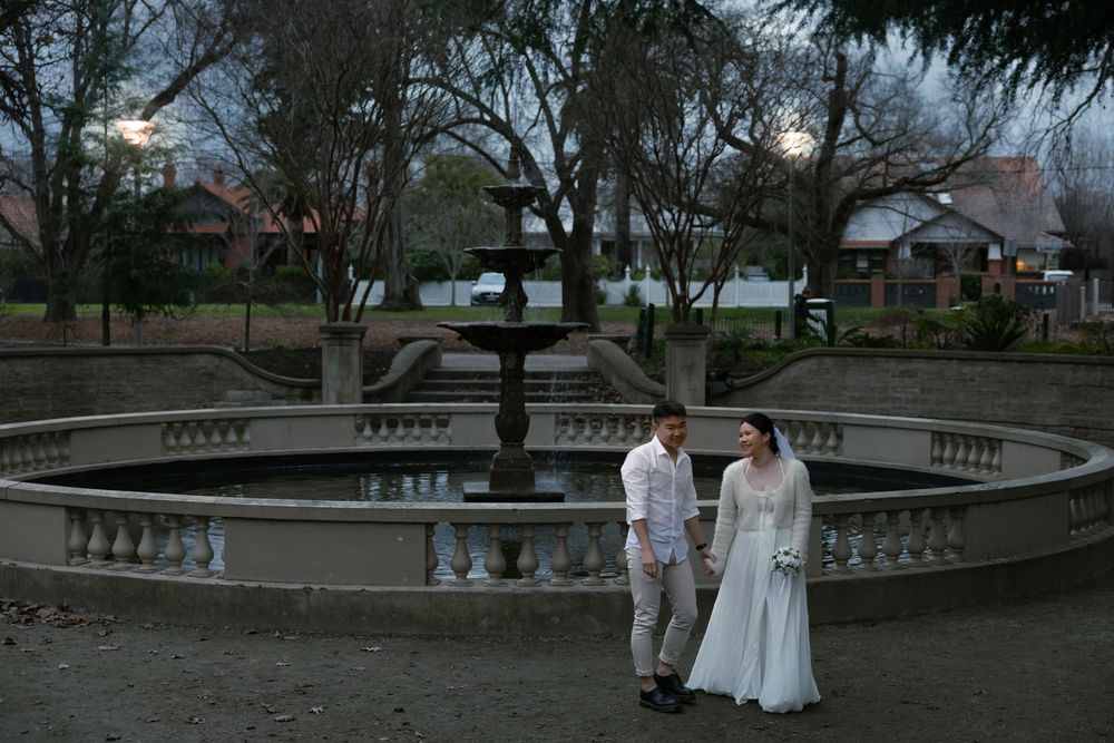 People in white stand on a classic stone terrace with ornate balustrades during a winter evening.