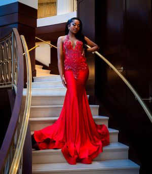 Someone wearing a stunning red mermaid gown with crystal details poses on an elegant staircase with gold railings.