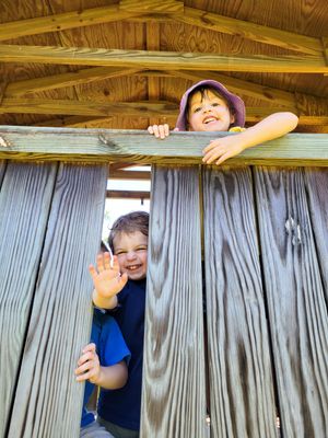 Kids playing peek-a-boo through wooden fence panels.