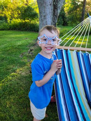 Child playing near a striped hammock in a sunny backyard.