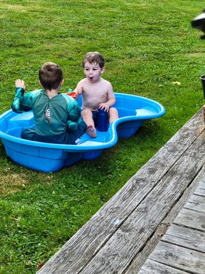 Children playing in a blue plastic pool on wooden deck.