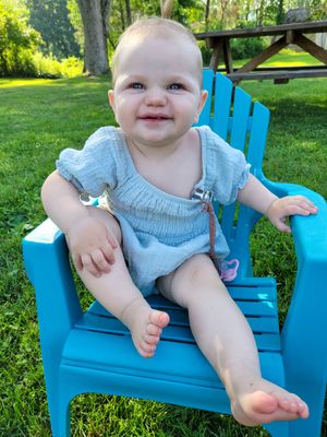 Baby sitting in bright blue Adirondack chair in sunny garden.