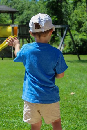 Child in blue shirt and khaki shorts playing in a sunny backyard.