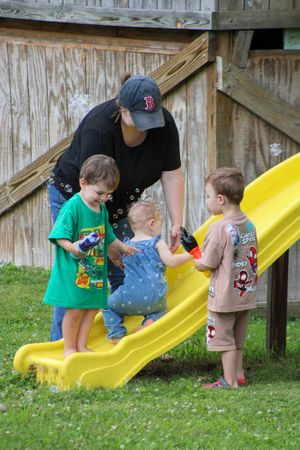 Children playing on a yellow slide in backyard with wooden fence.