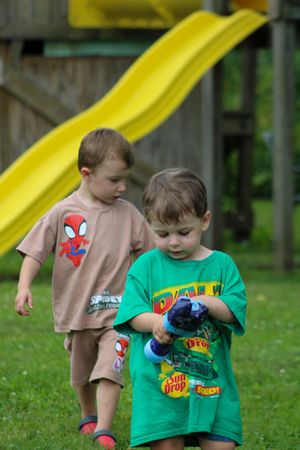 Two children in casual clothing play together on a grassy lawn with toys.