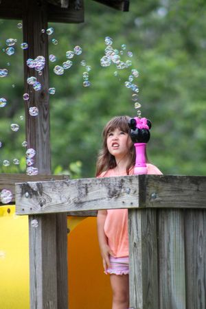 Soap bubbles float around a wooden deck railing on a sunny day.