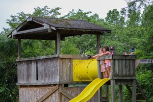 Wooden playground structure with yellow slide in a backyard setting.
