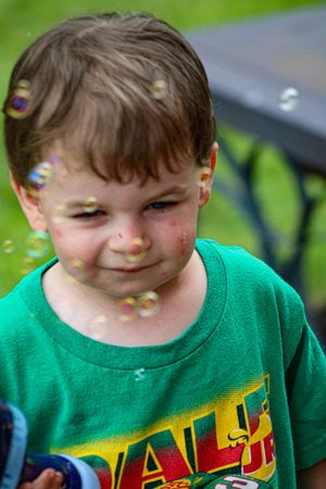Child in bright green t-shirt plays with bubbles outdoors.