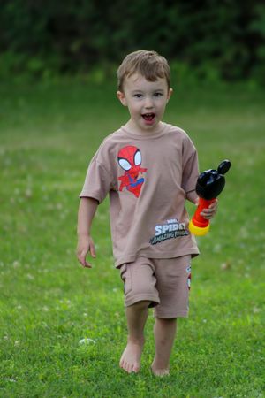 Small child in beige outfit runs across green grass while playing.