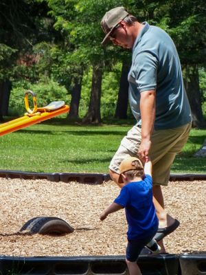 Adult and child playing together on playground equipment with wood chips on the ground.