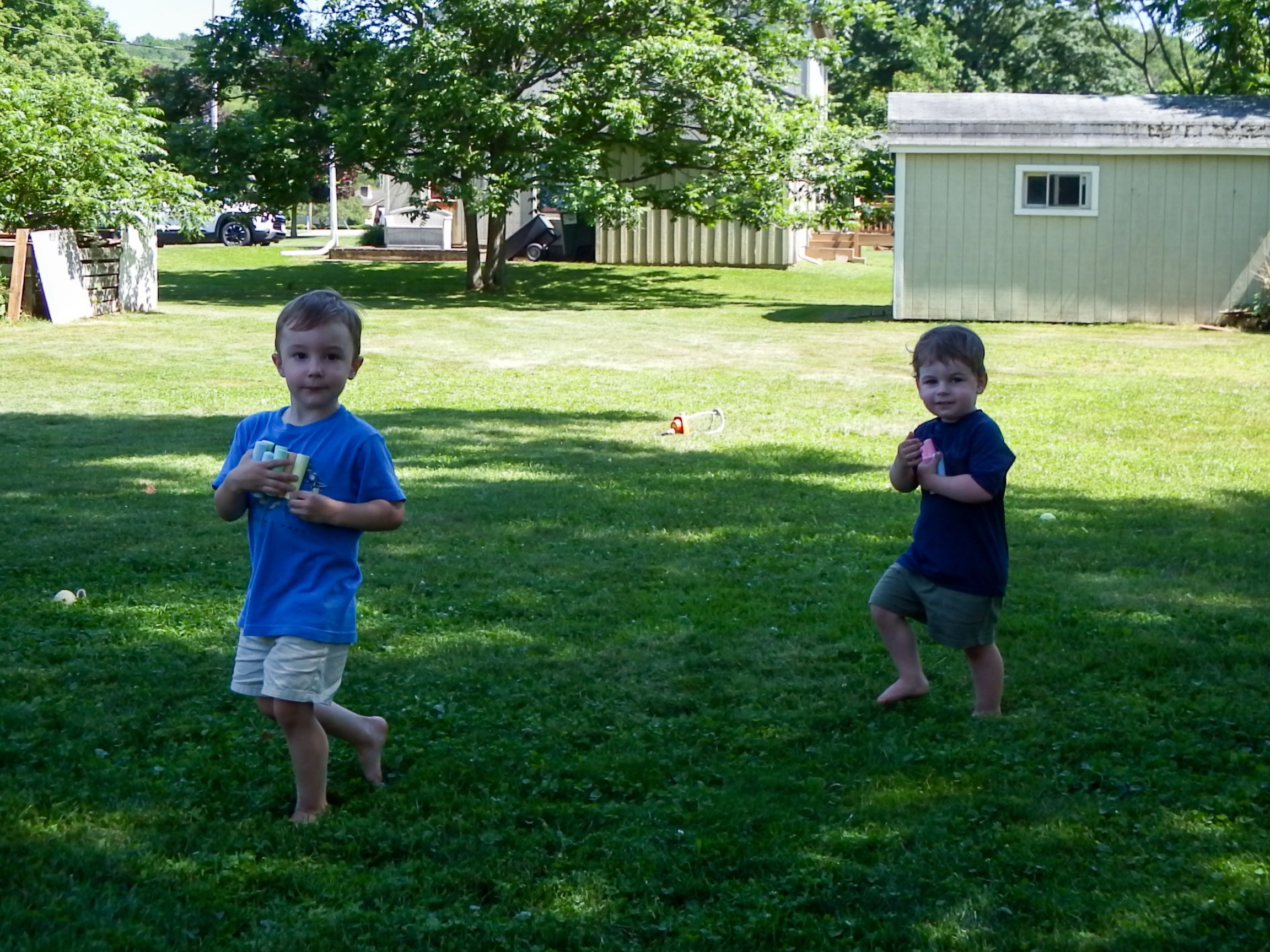 Young child plays and runs through a grassy backyard on a sunny summer day.