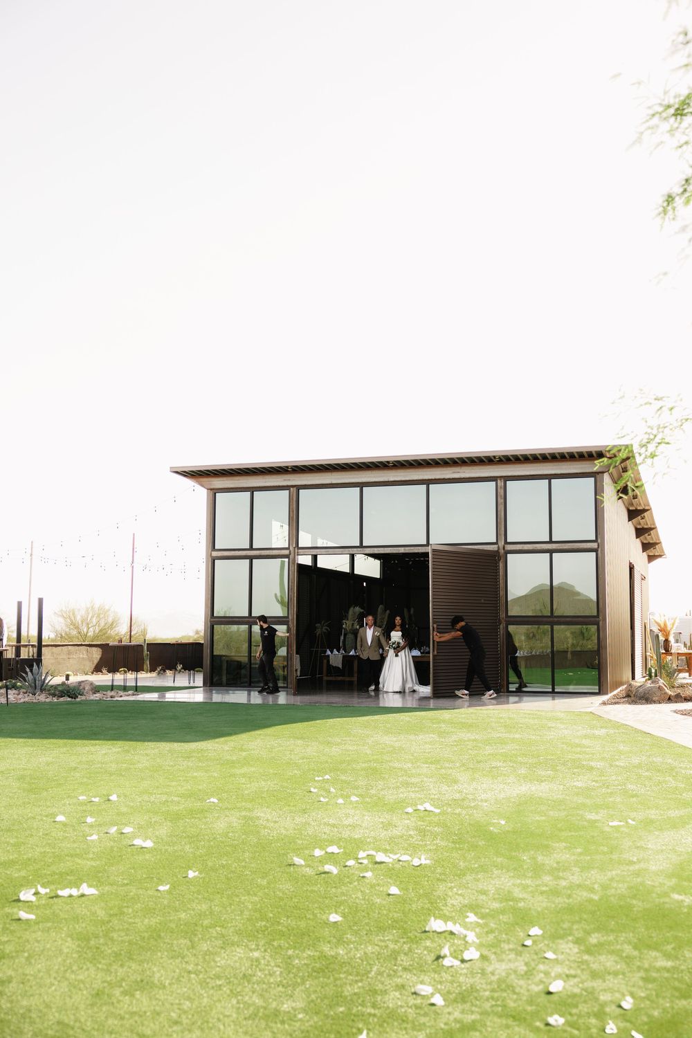 Wide view of modern wedding venue with green lawn and scattered flower petals.