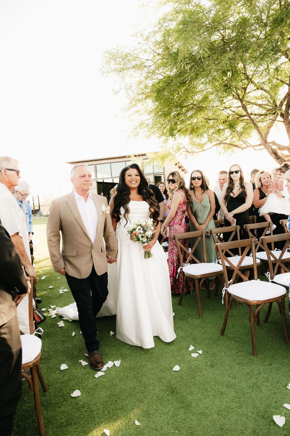 Wedding ceremony setup with wooden chairs and scattered petals on artificial grass.
