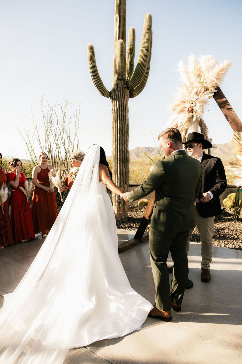Desert wedding ceremony with saguaro cactus and flowing white dress in sunlight.