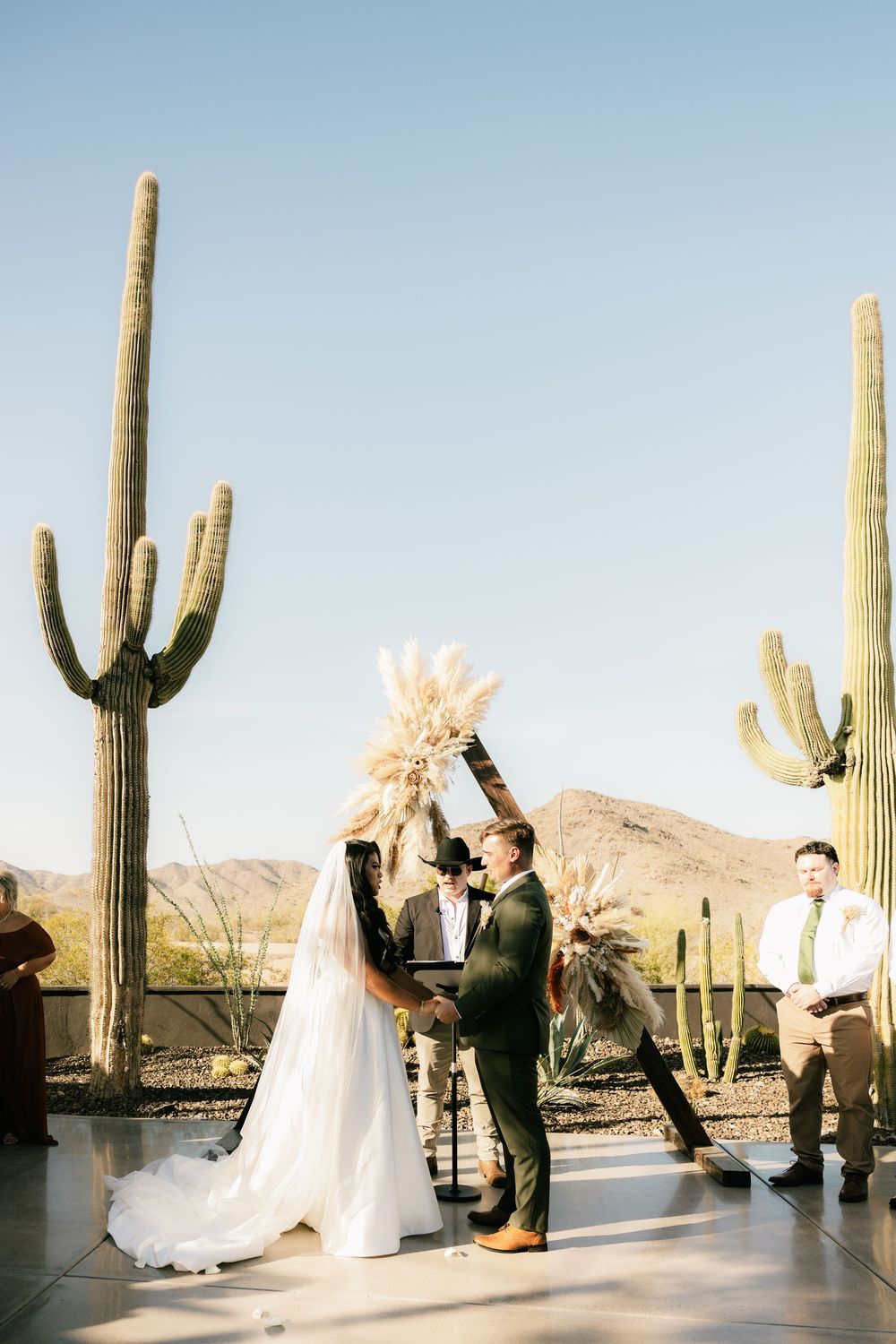 Wedding ceremony against desert landscape with tall saguaro cacti and mountain backdrop.