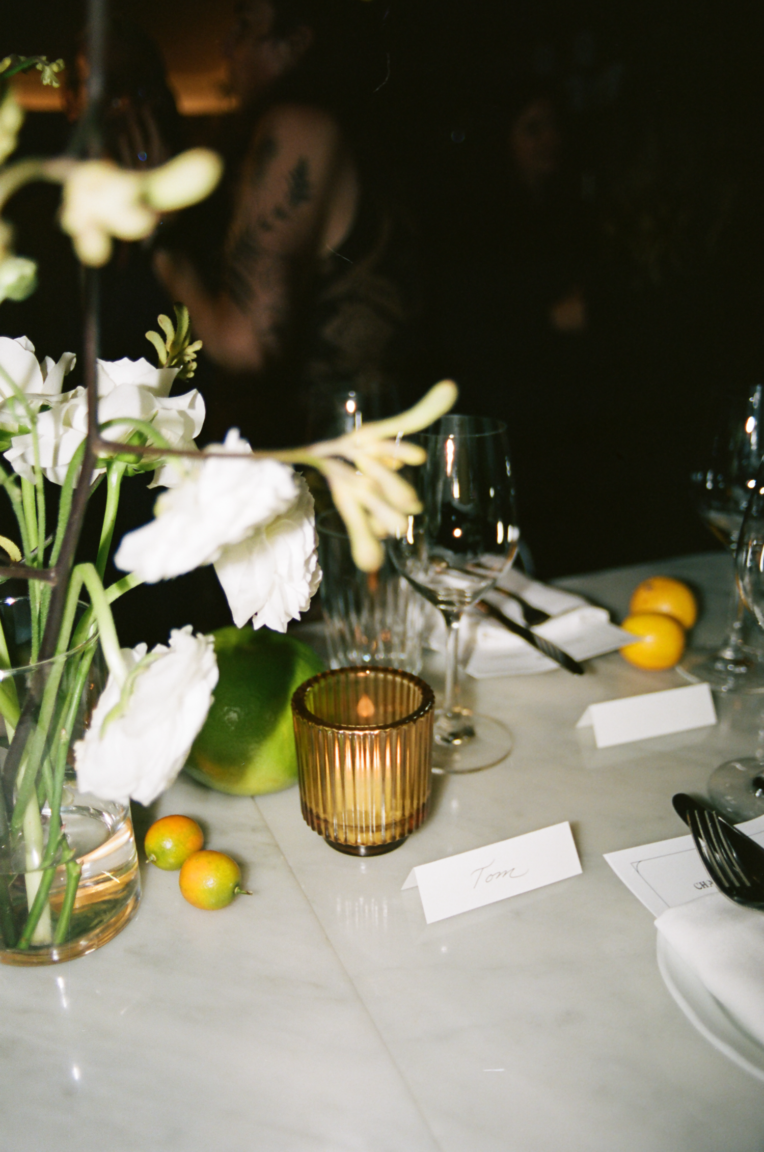 An elegant wedding table setting with citrus accents, white flowers, and amber glass votives.