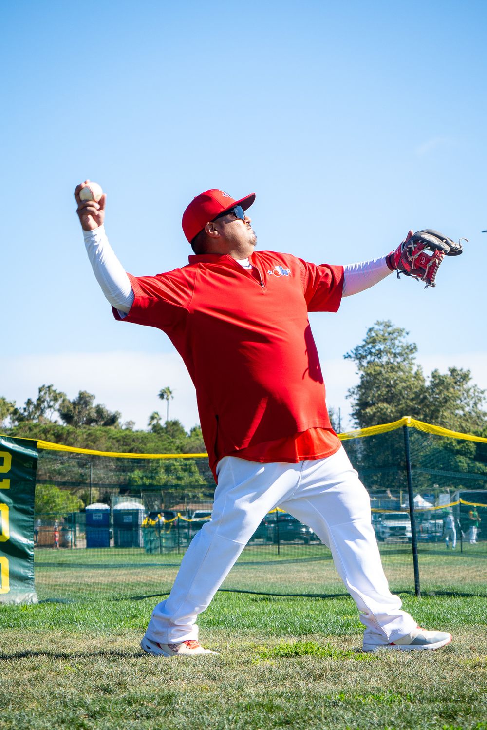 Baseball coach demonstrating pitching technique on sunny practice field.