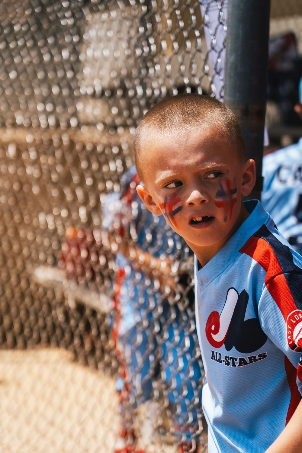 Young baseball player watching game through chain link fence.