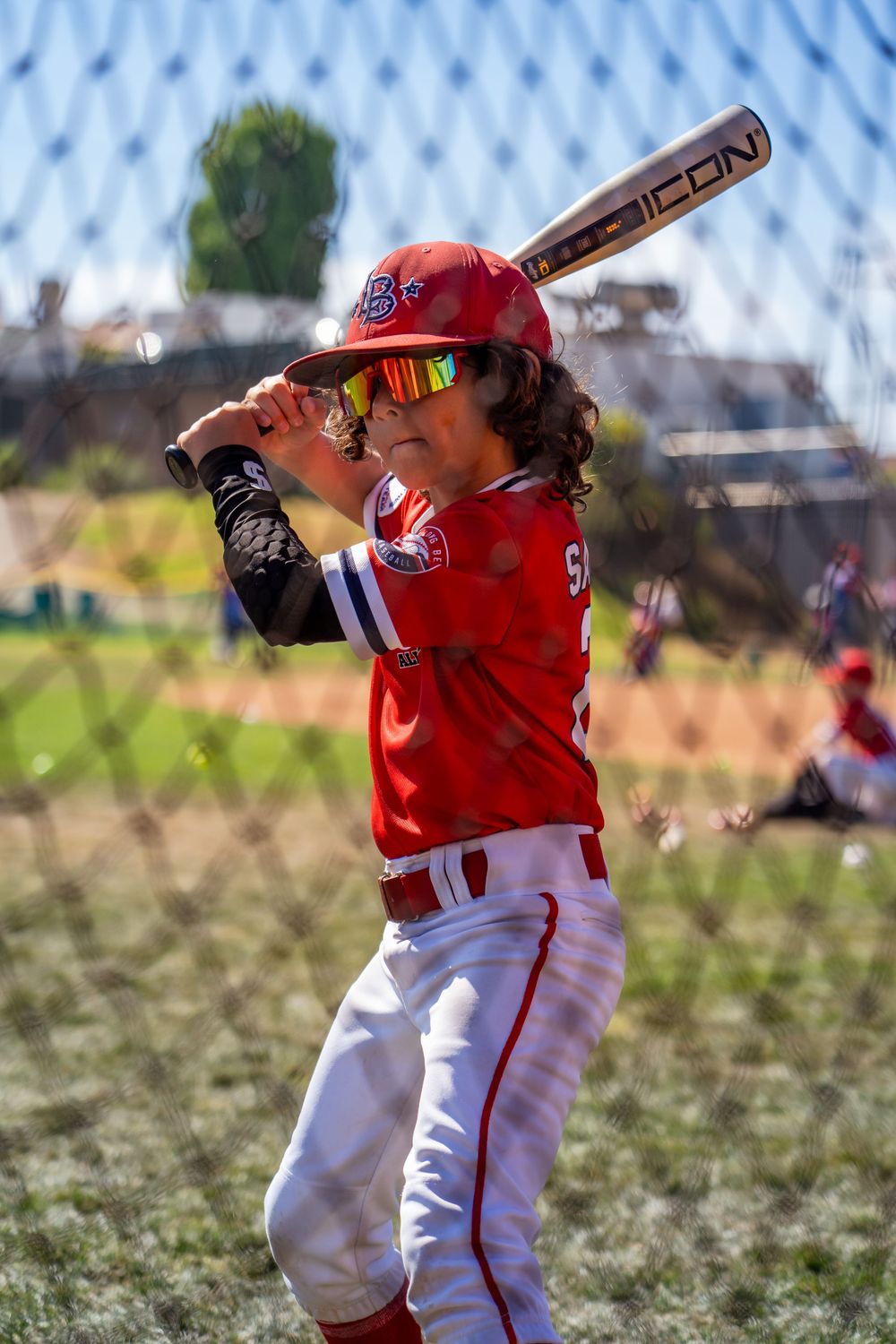 Youth baseball player in red uniform taking batting stance on field.