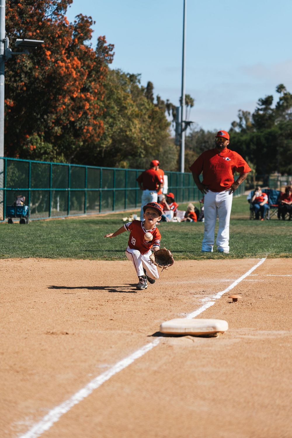 Small baseball player fielding ground ball near first base during practice.