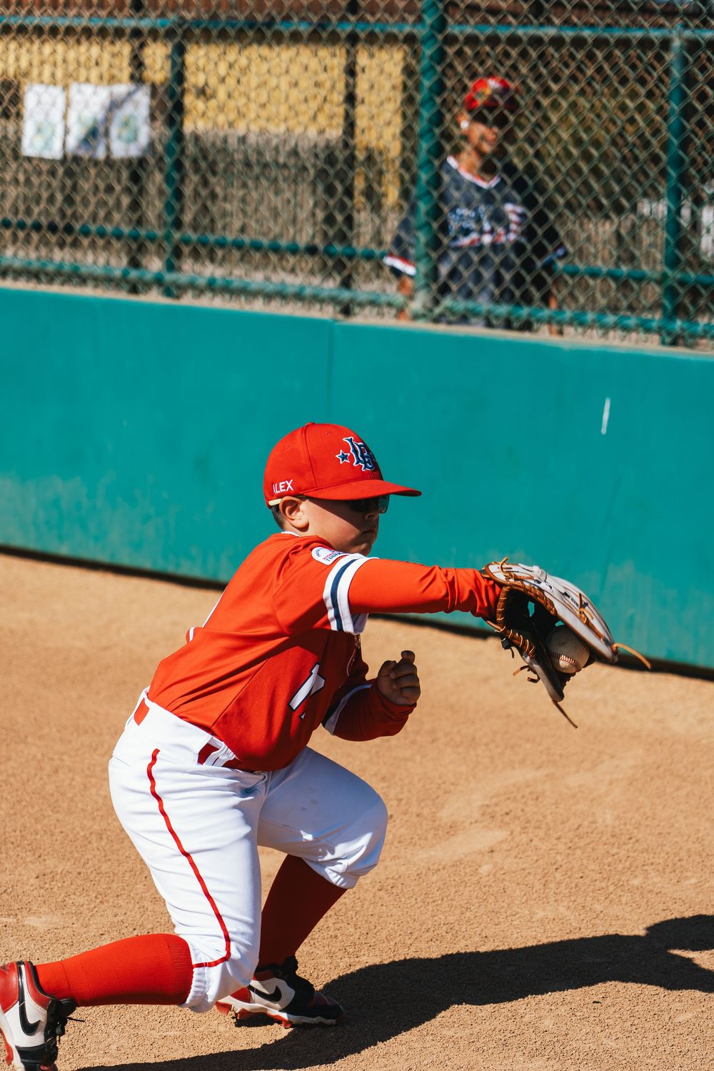 Youth baseball player in red uniform crouching in fielding position on baseball diamond.