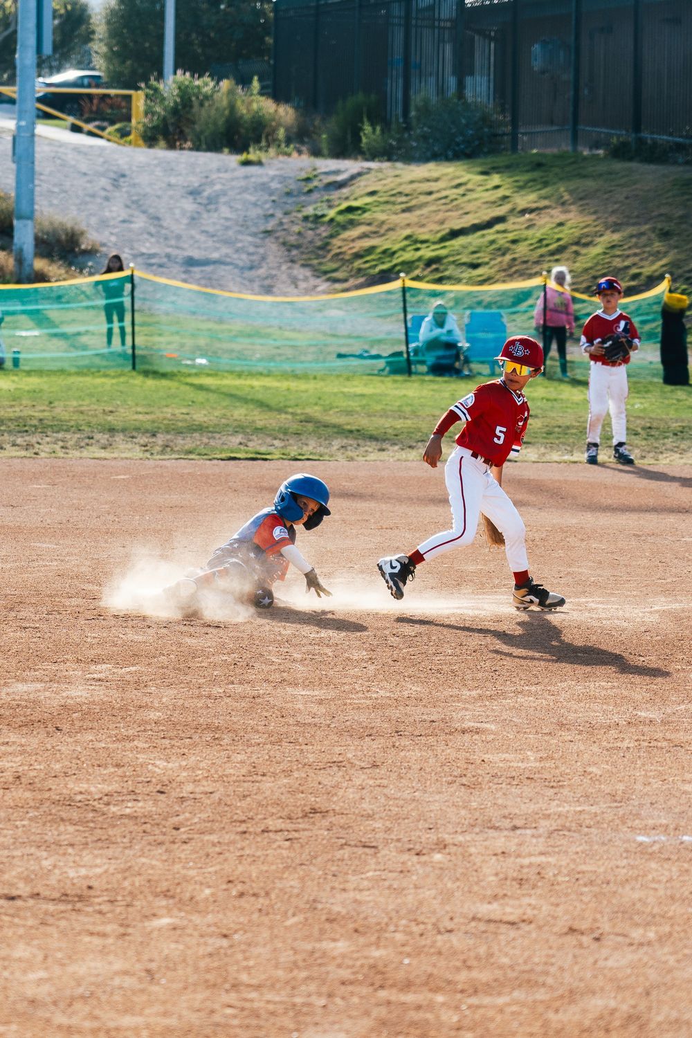 Baseball play at home plate with sliding runner creating dust cloud.