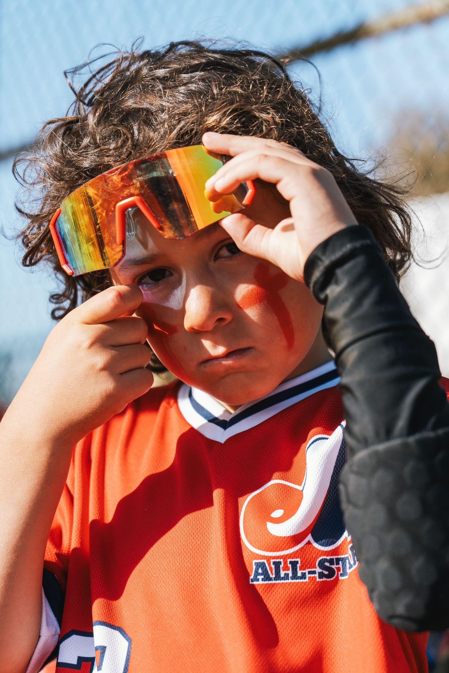Young athlete adjusts colorful sports goggles while wearing orange All-Star jersey outdoors.