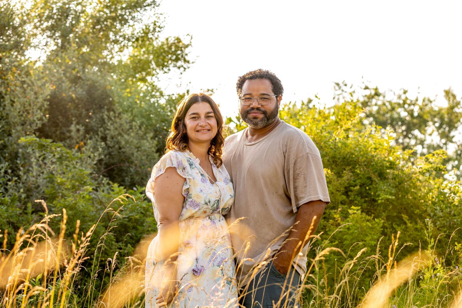 Couple smiling together in sunlit meadow with golden grass.
