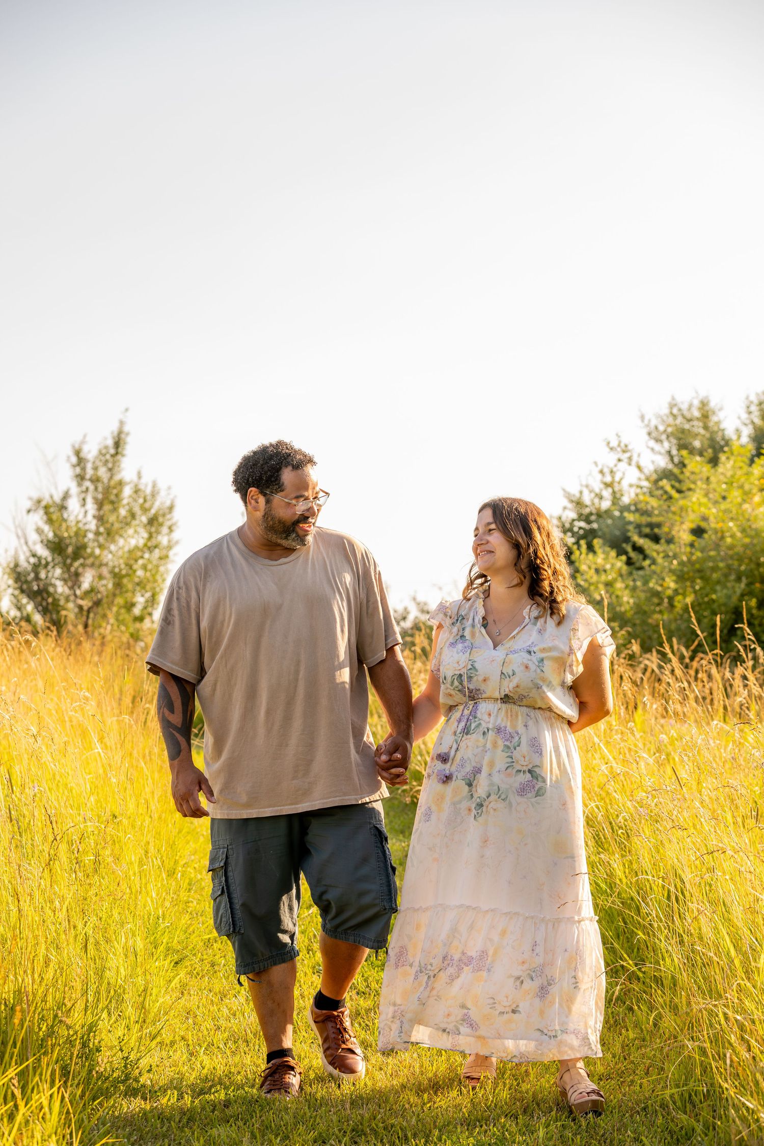Couple walking through golden field of tall grass at sunset sharing a romantic moment.