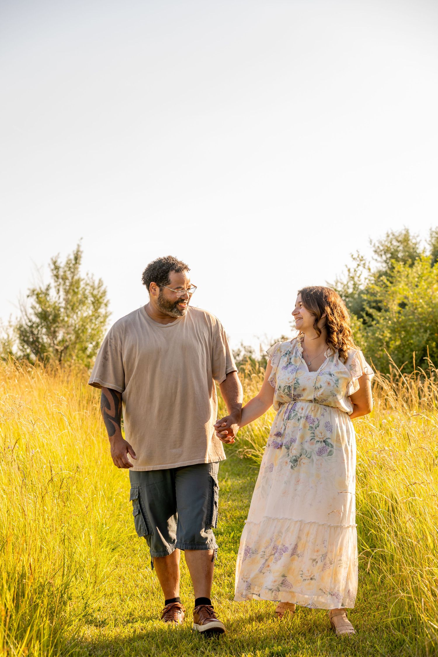 Couple walking together in a sunlit meadow with tall yellow grass.