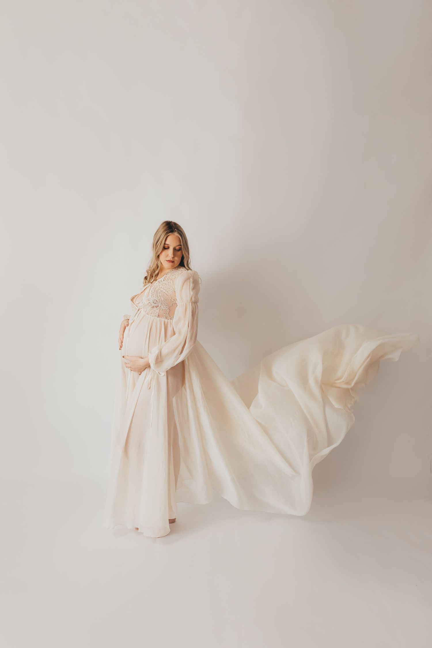 Romantic maternity portraits in flowing blush gown with dramatic fabric movement.