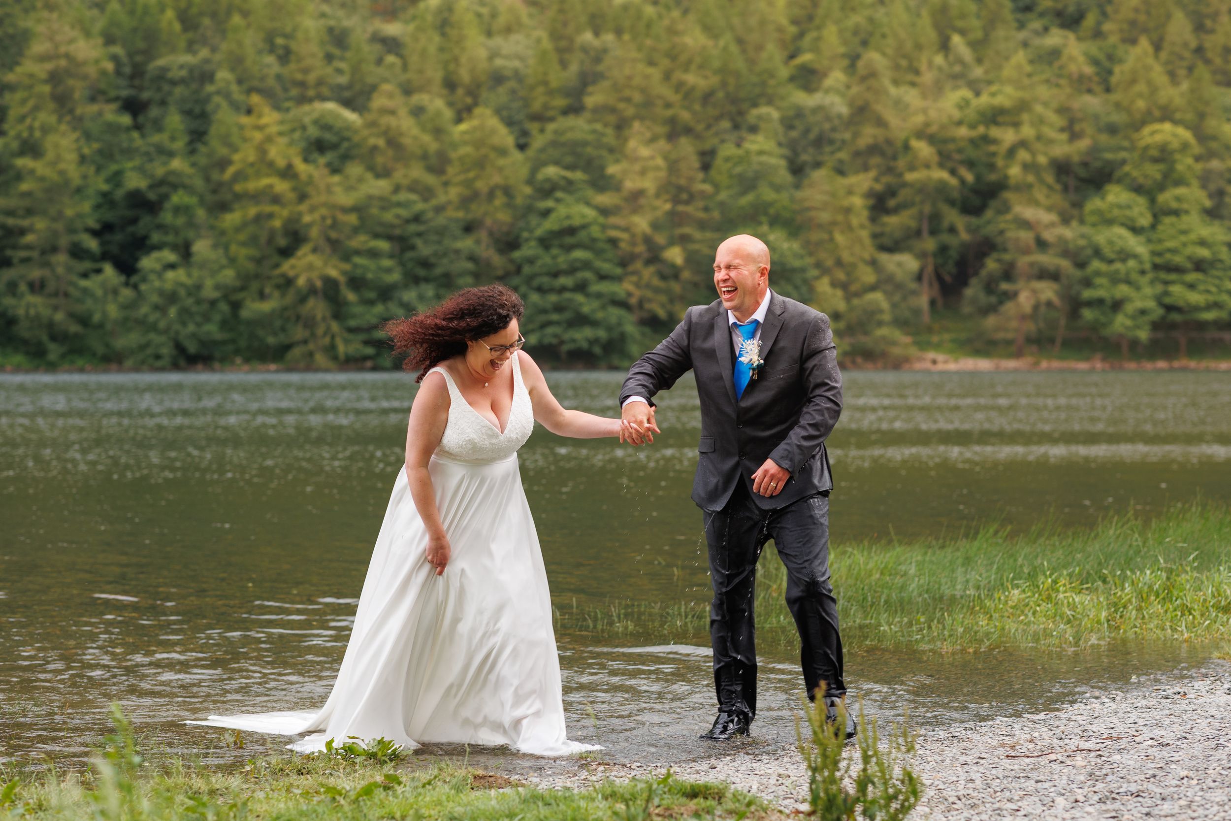 A couple shares a joyful moment together by a serene lake surrounded by lush green forest.