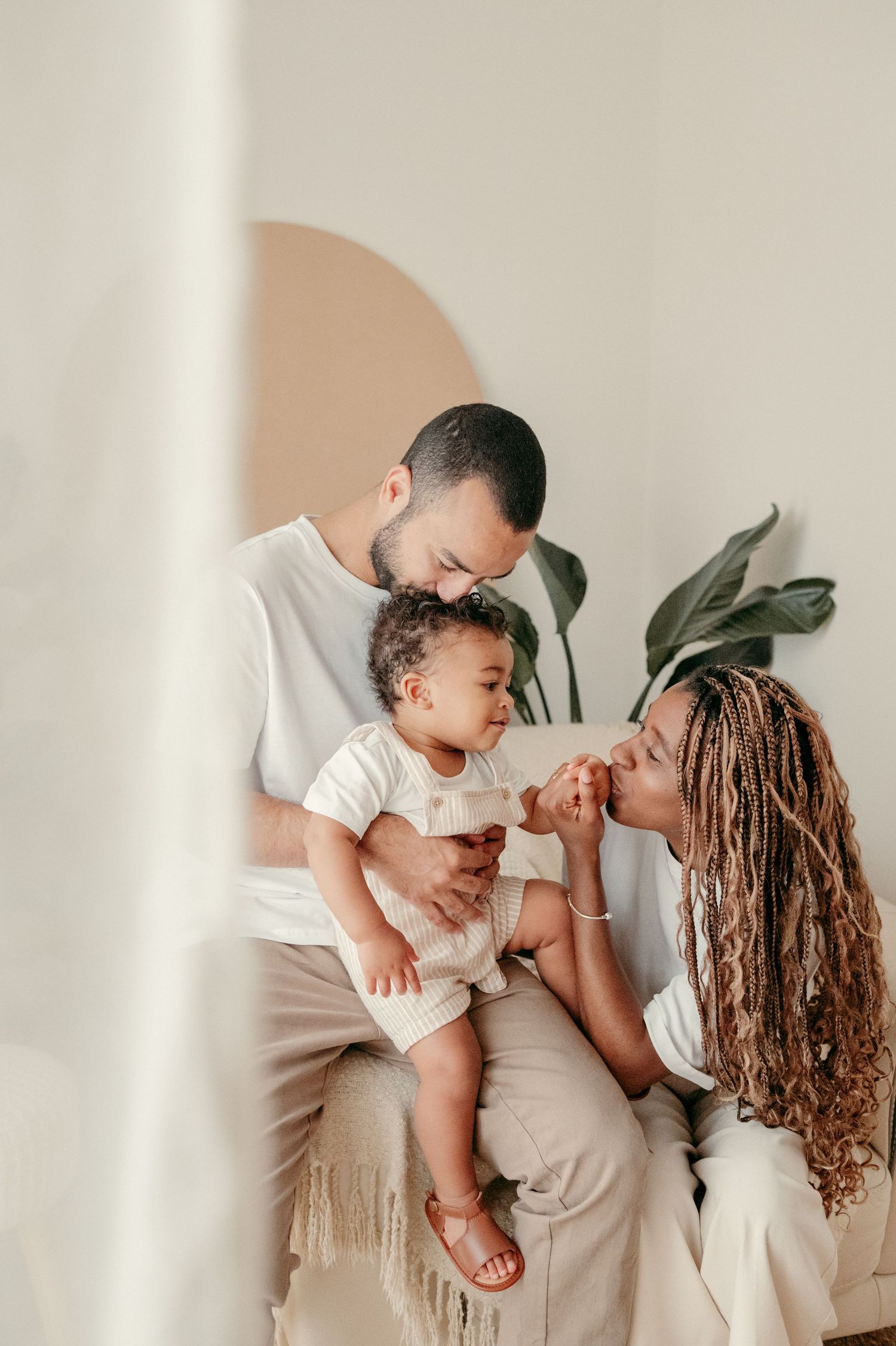 Family sharing tender moment together against white wall with indoor plant.