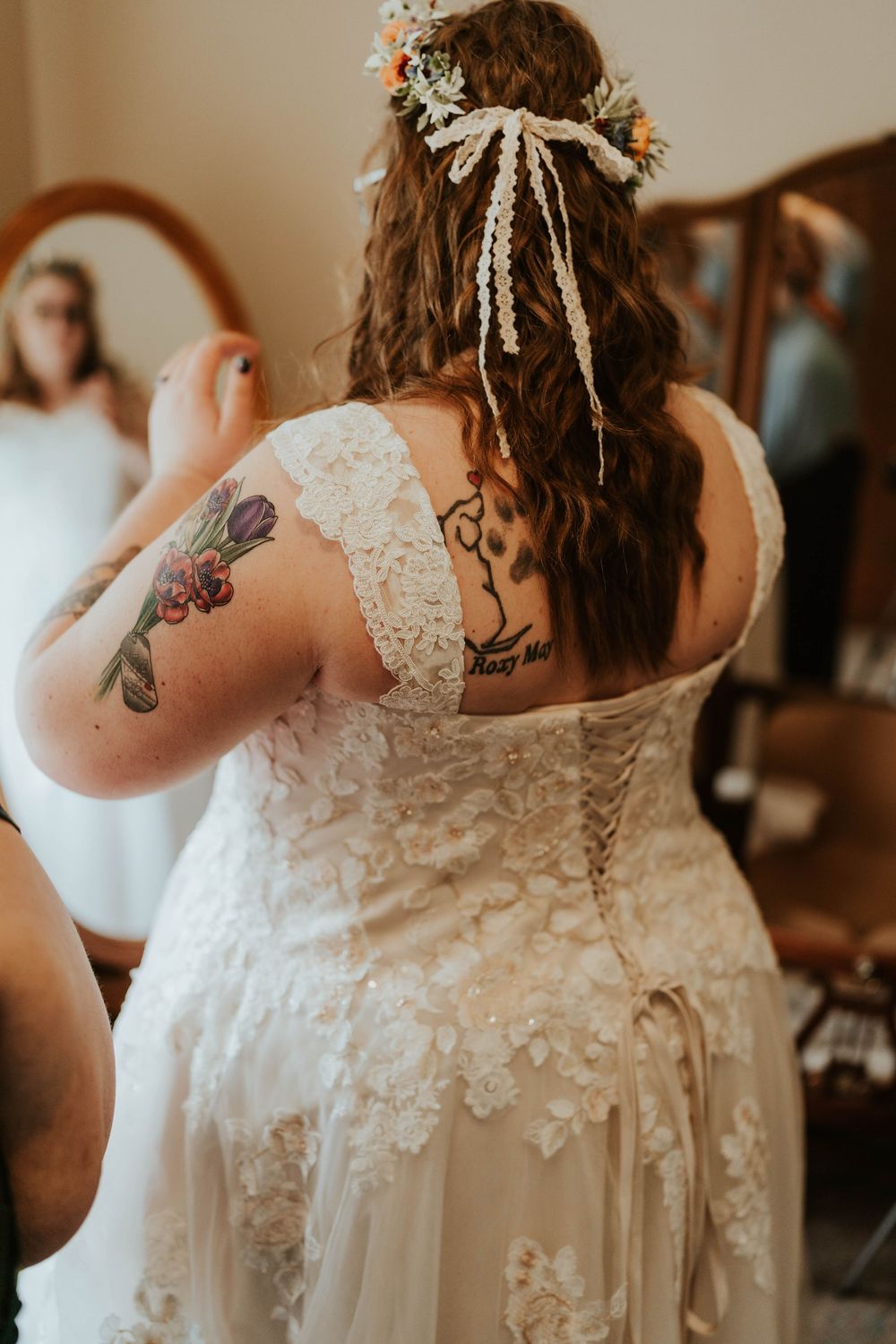 Back view of bride in lace wedding gown with floral crown and colorful tattoos on shoulder and back.
