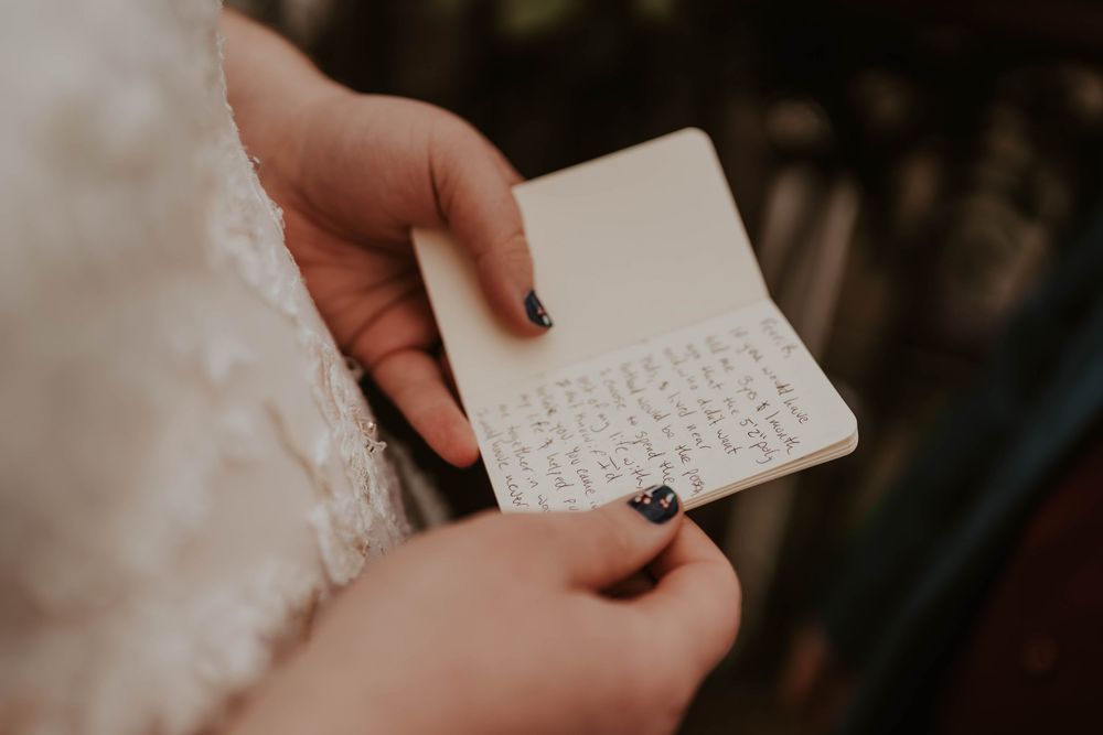 Close-up of a bride holding a small notebook with handwritten wedding vows, navy nail polish visible.