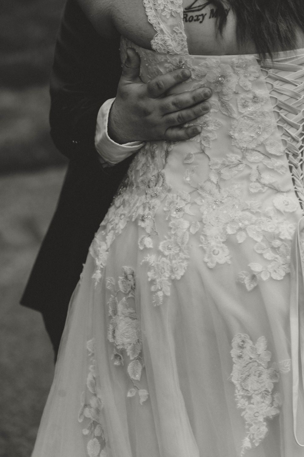 Close-up black and white photo of groom's hand on bride's lace wedding dress with corset back detail.