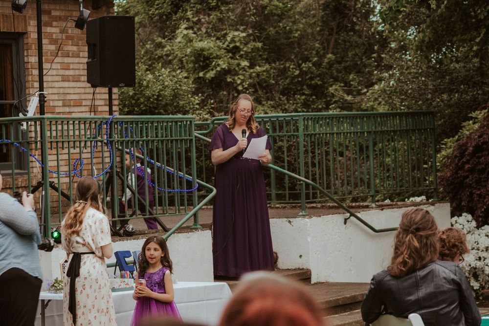A woman in a purple gown officiates an outdoor wedding ceremony while guests are seated.