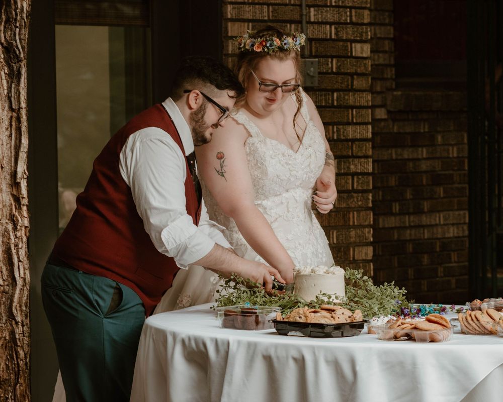 Bride and groom cutting wedding cake together at rustic indoor reception venue with brick wall.