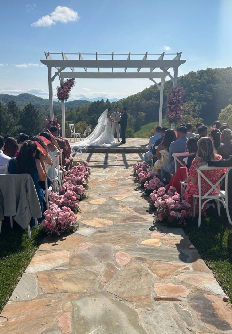 An outdoor wedding ceremony setup with white chairs and a wooden arch adorned with flowers overlooking a mountain vista.