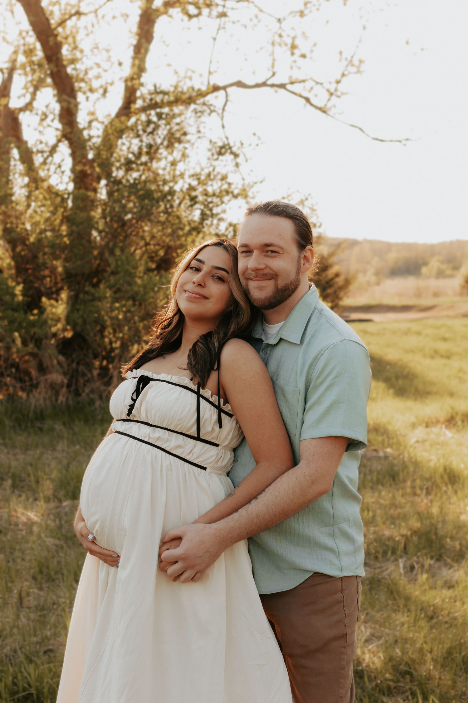 Couple standing in Minnesota field smiling as man holds womans pregnant belly