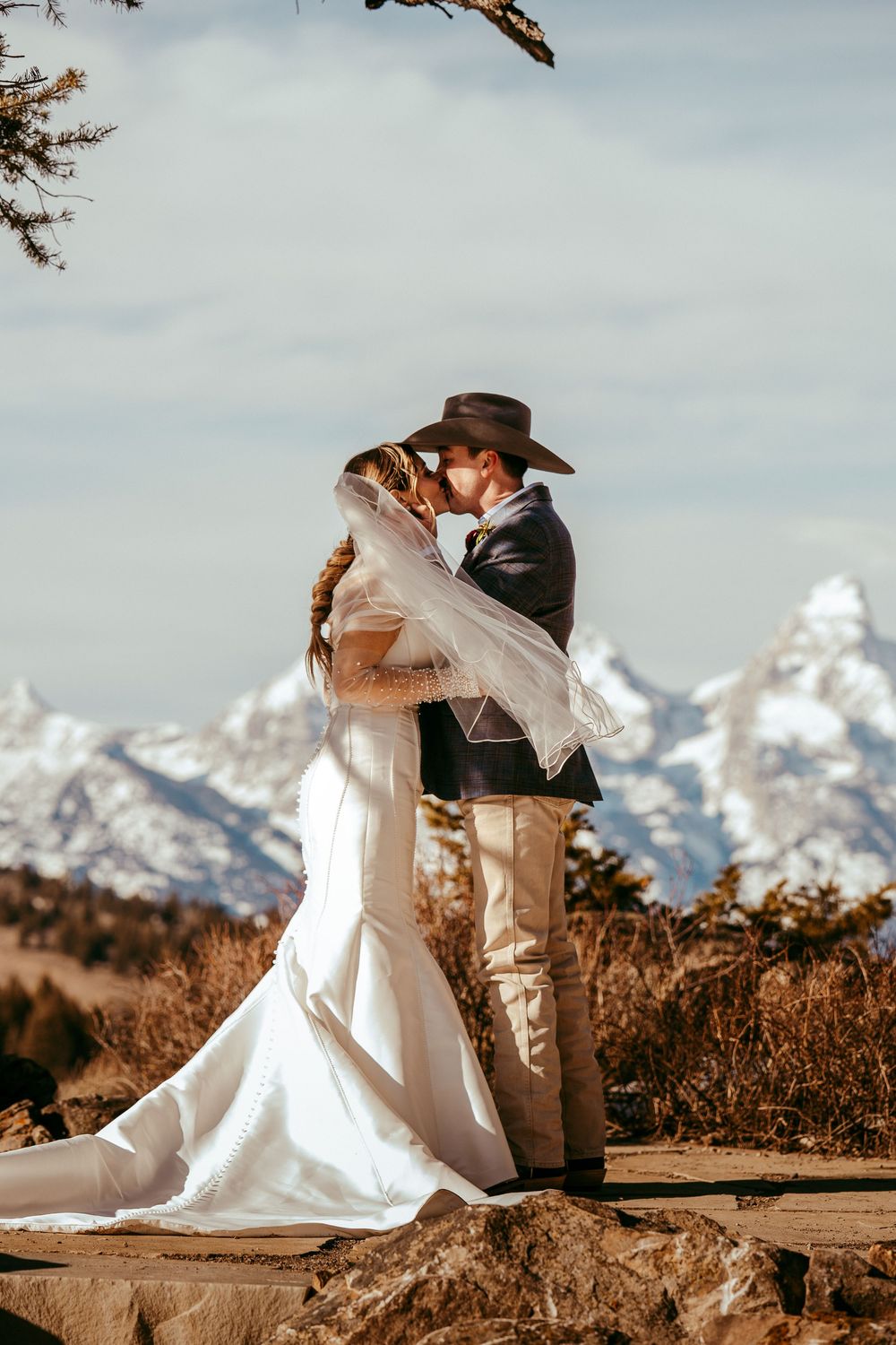 Romantic winter mountain wedding portrait of a bride and groom in a snowy landscape at golden hour.