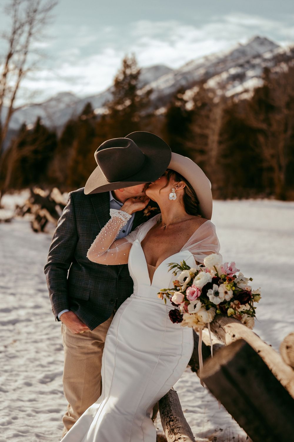 Romantic winter mountain wedding portrait of a bride and groom in a snowy landscape at golden hour.