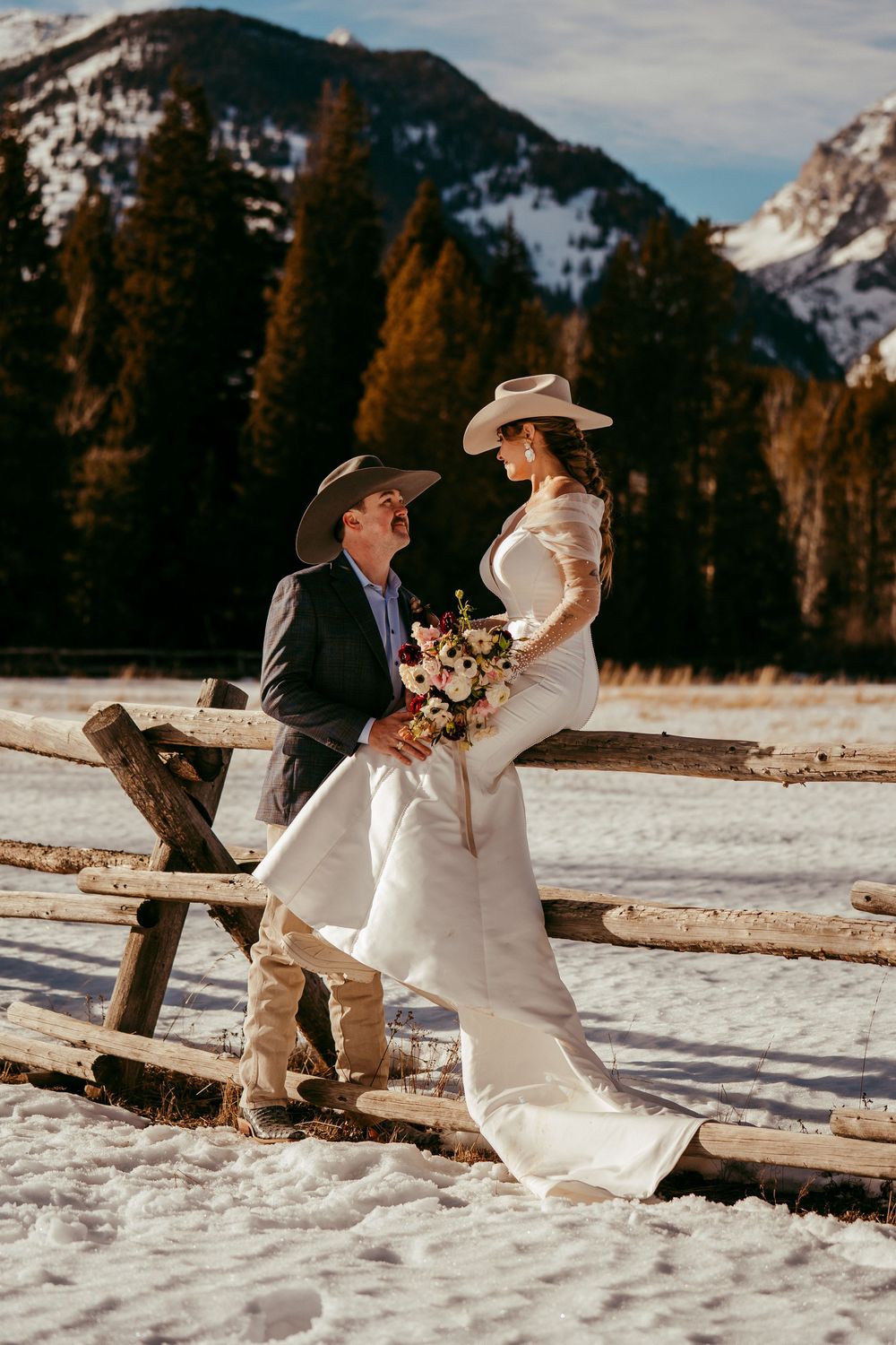 Romantic winter mountain wedding portrait of a bride and groom in a snowy landscape at golden hour.
