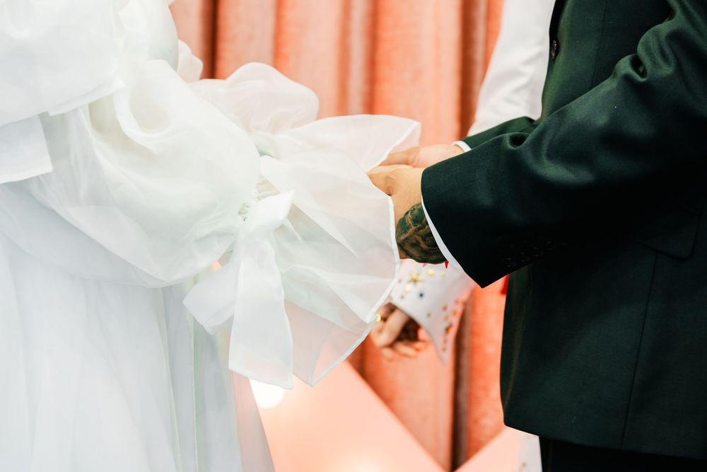 Close-up of bride and groom holding hands during wedding ceremony with white bow detail.